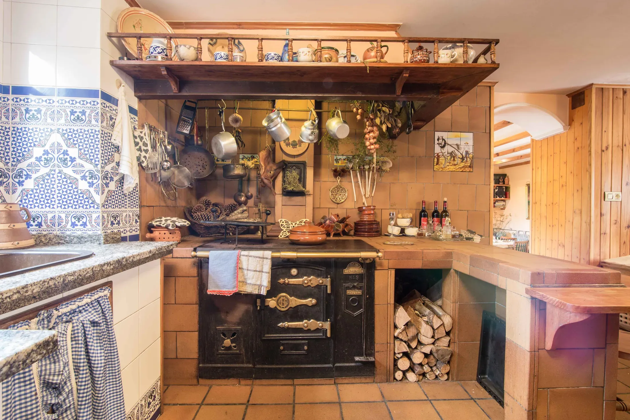 Kitchen corner with a wood-fired range, hanging copper pots and stacked firewood