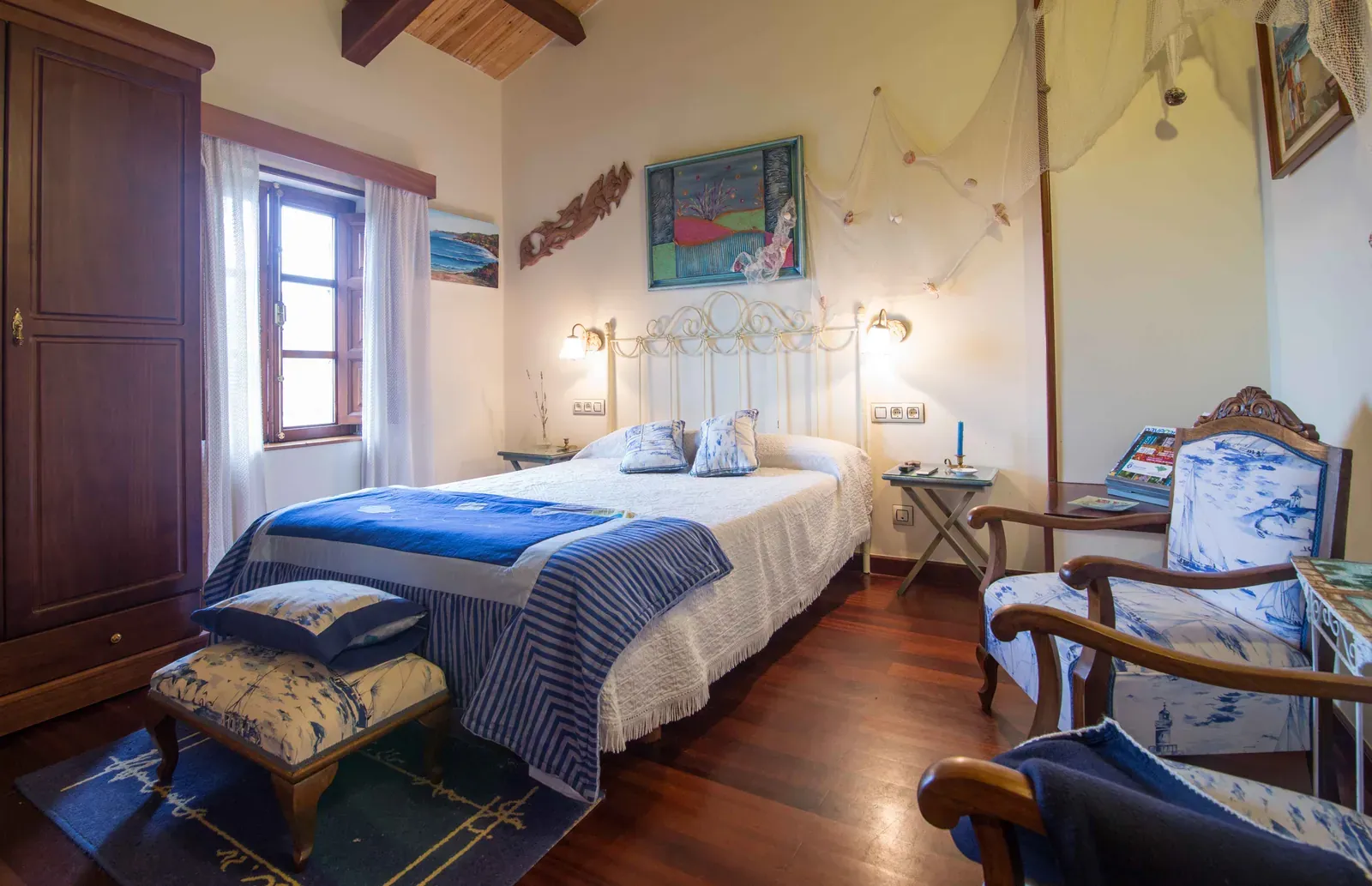 Habitación individual con colcha azul y sillón junto a la ventana
